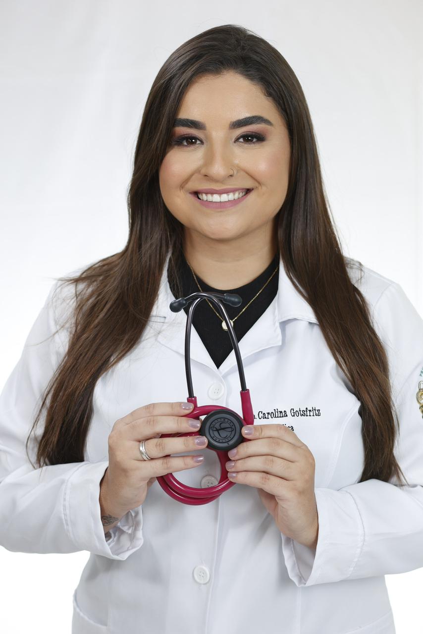 Dra. Carolina Gotsfritz, médica, sorrindo com jaleco branco e estetoscópio.